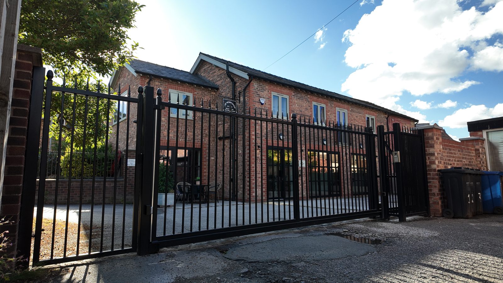 The black courtyard gates closed across the drive, with the brick building behind them.