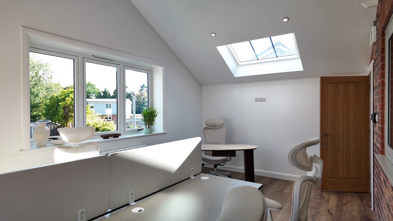 Office 5, on the first floor: screened white desks and cream chairs under a vaulted ceiling, lit by a skylight and a window over the rooftops.