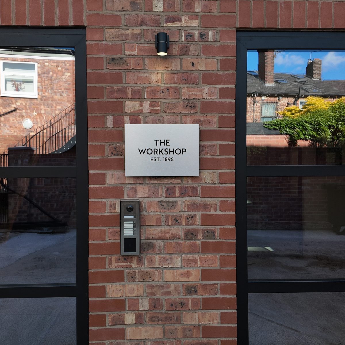 The plaque at the door - The Workshop, est. 1898 - above the camera intercom on brick.