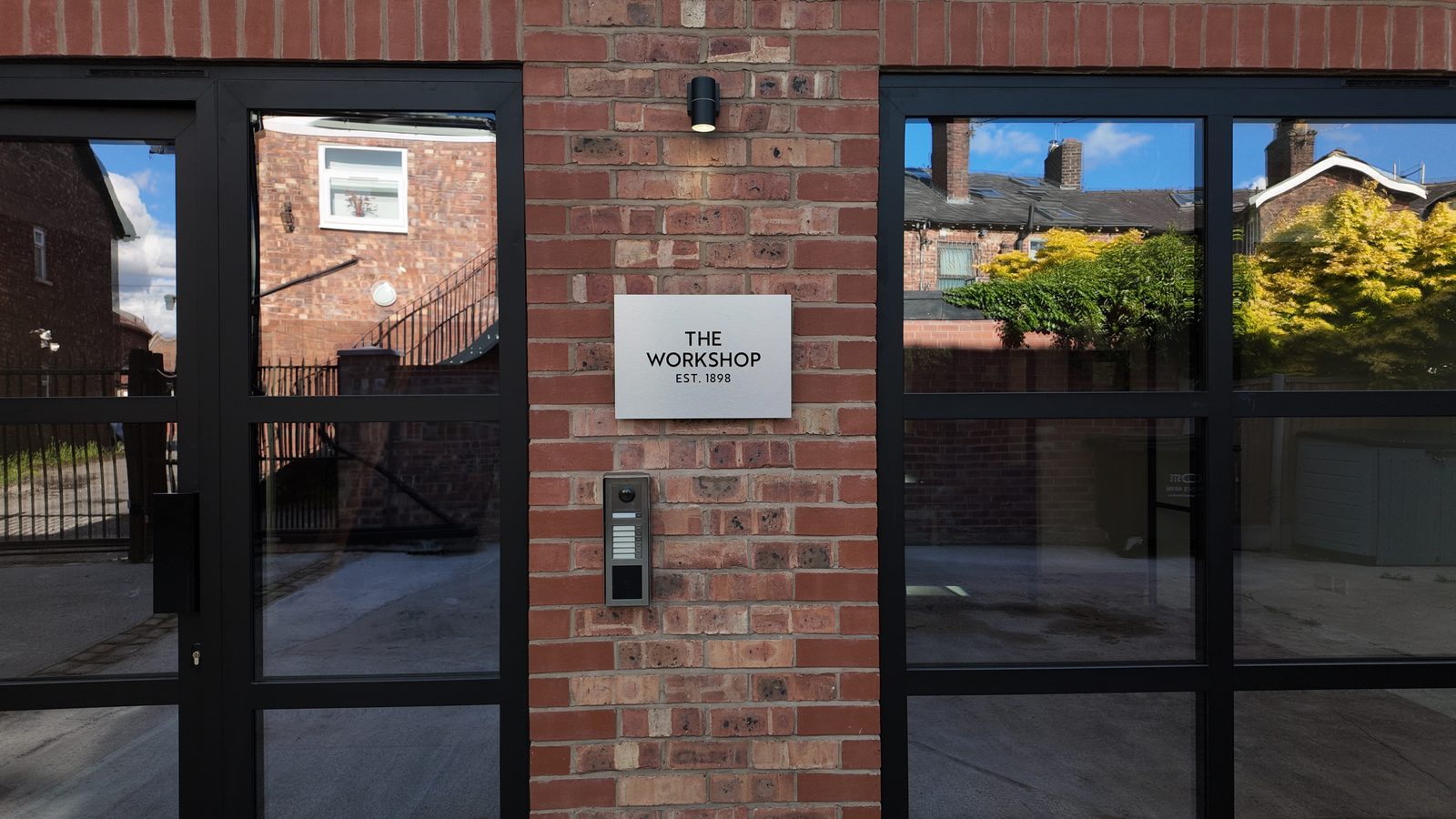 The plaque at the door - The Workshop, est. 1898 - above the camera intercom on brick, between two glazed doors.