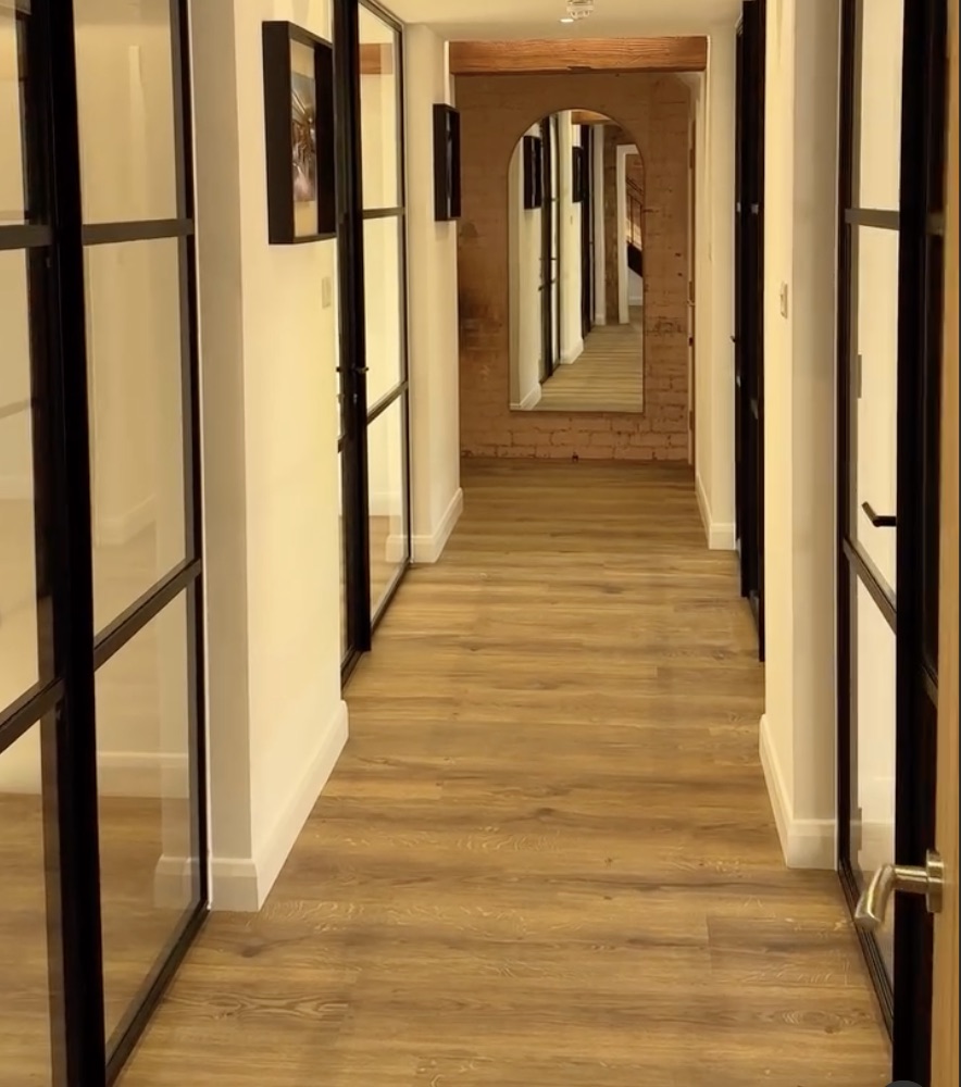 The corridor in evening light, with glazed partitions either side and an arched mirror on brick at the end.
