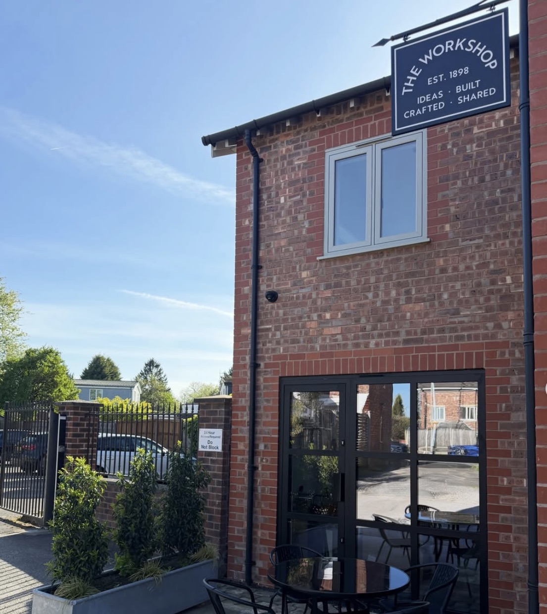 The entrance to The Workshop: the navy hanging sign above a black-framed glazed door, with the gates and a bistro table in front.