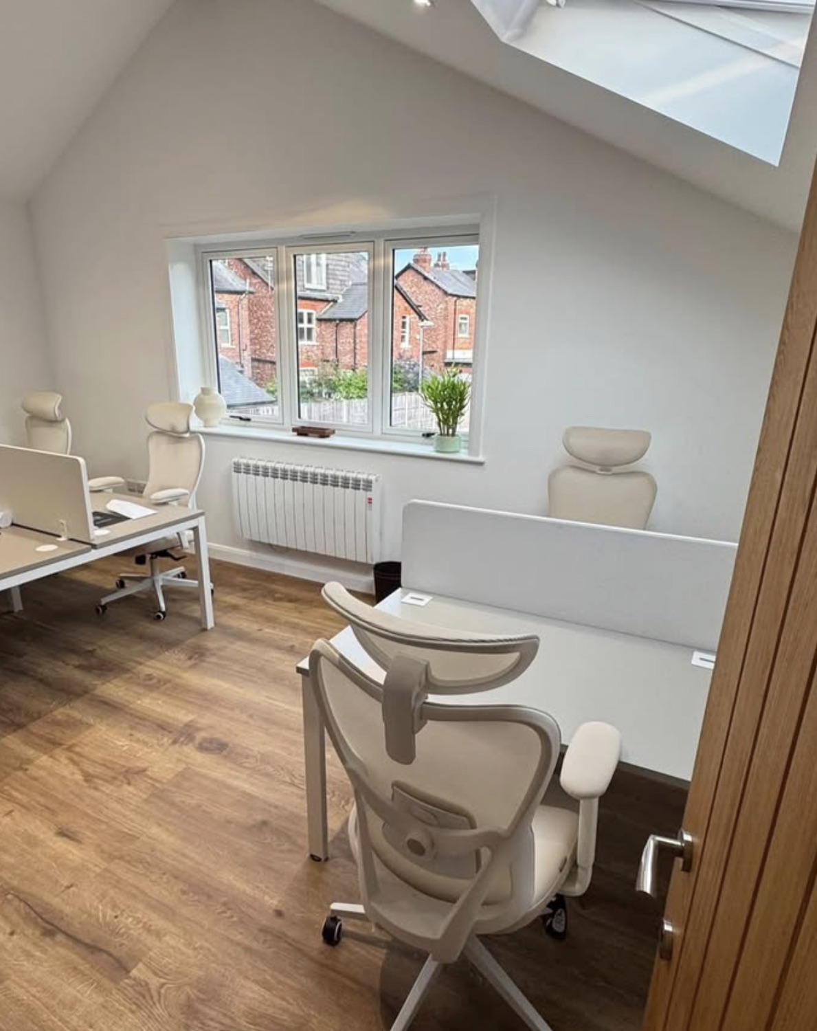 An office room seen from its doorway, lit by a skylight and a window facing the neighbouring terraces.