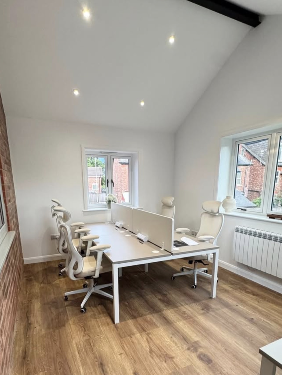A bright office room in the building, with white walls, a vaulted ceiling, exposed brick to one side and a bank of white desks.