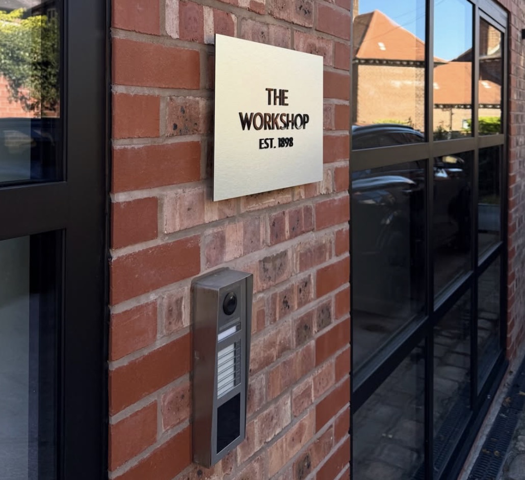 The cream wall plaque reading The Workshop, Est. 1898, above the camera intercom on brick.