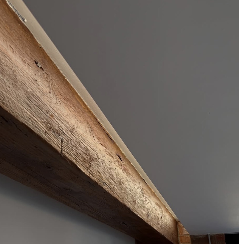 A reclaimed timber beam against a grey wall, its grain lit from below.
