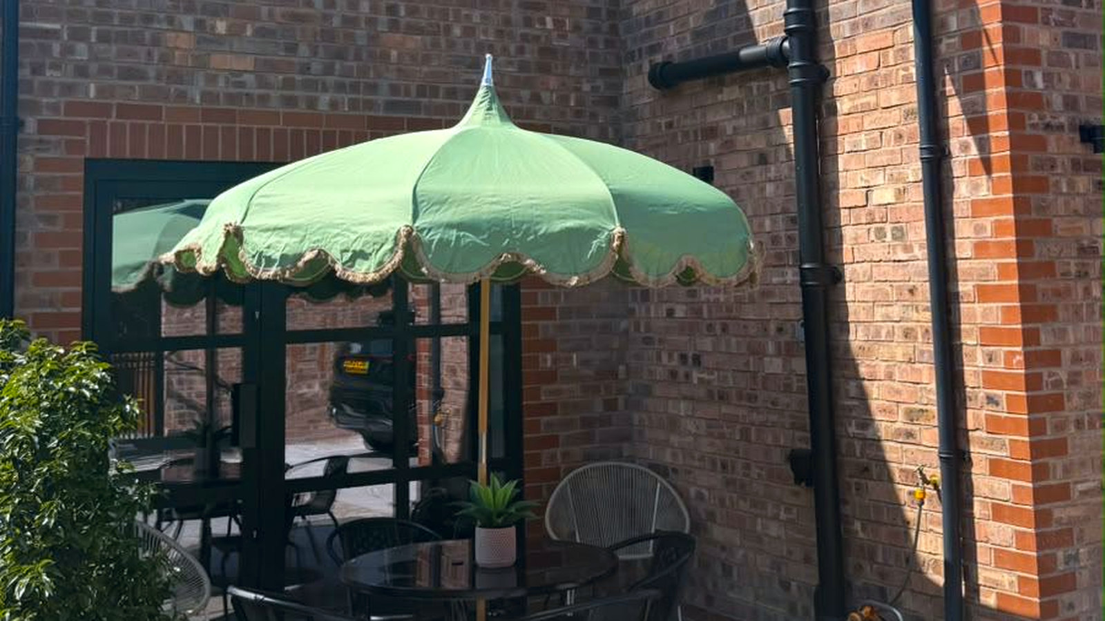 The courtyard with the sage umbrella up over a bistro table and chairs, against the brick and courtyard doors.